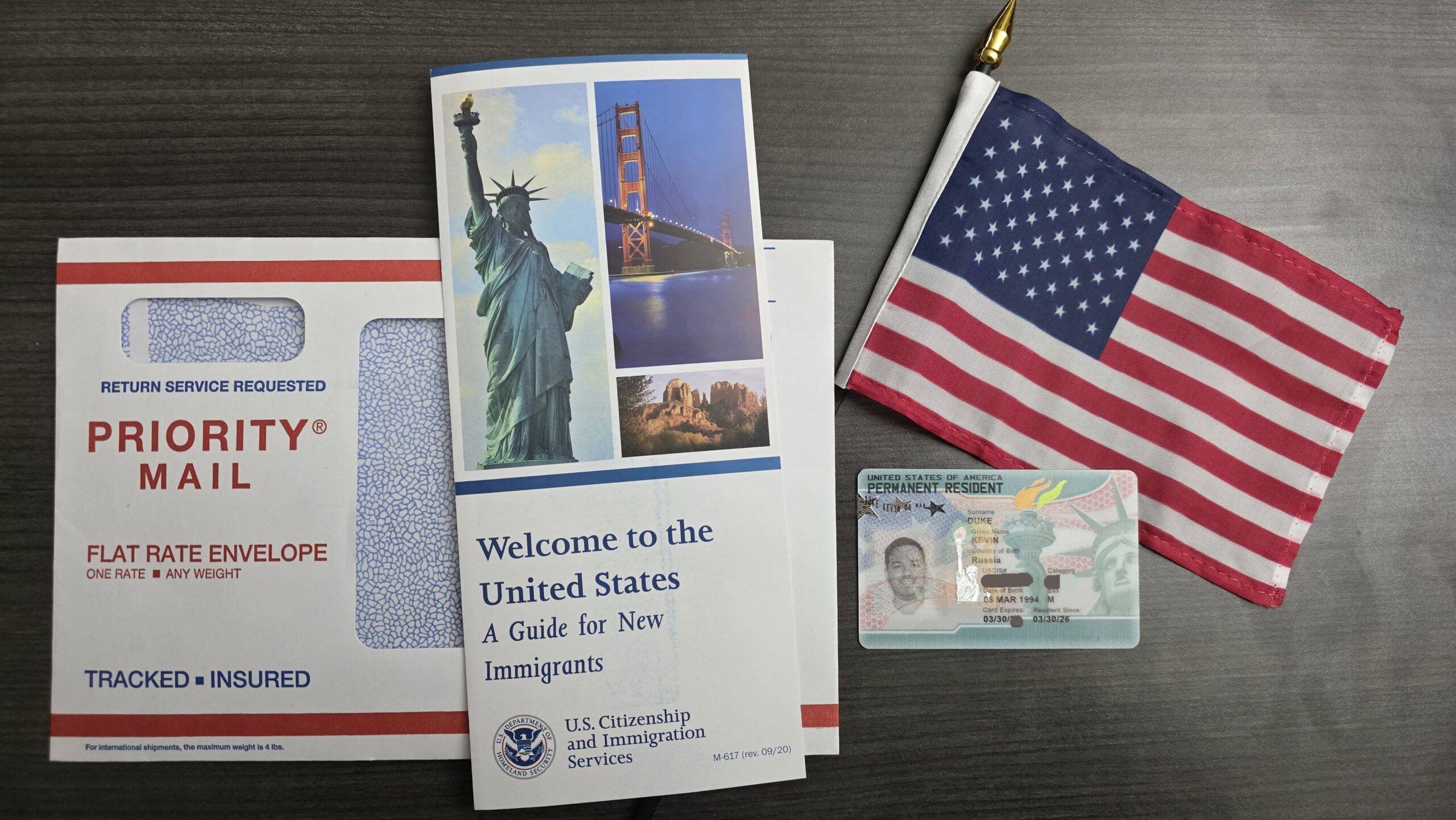 Грин-карта Кевина Дюка и приветственные материалы USCIS рядом с флагом США