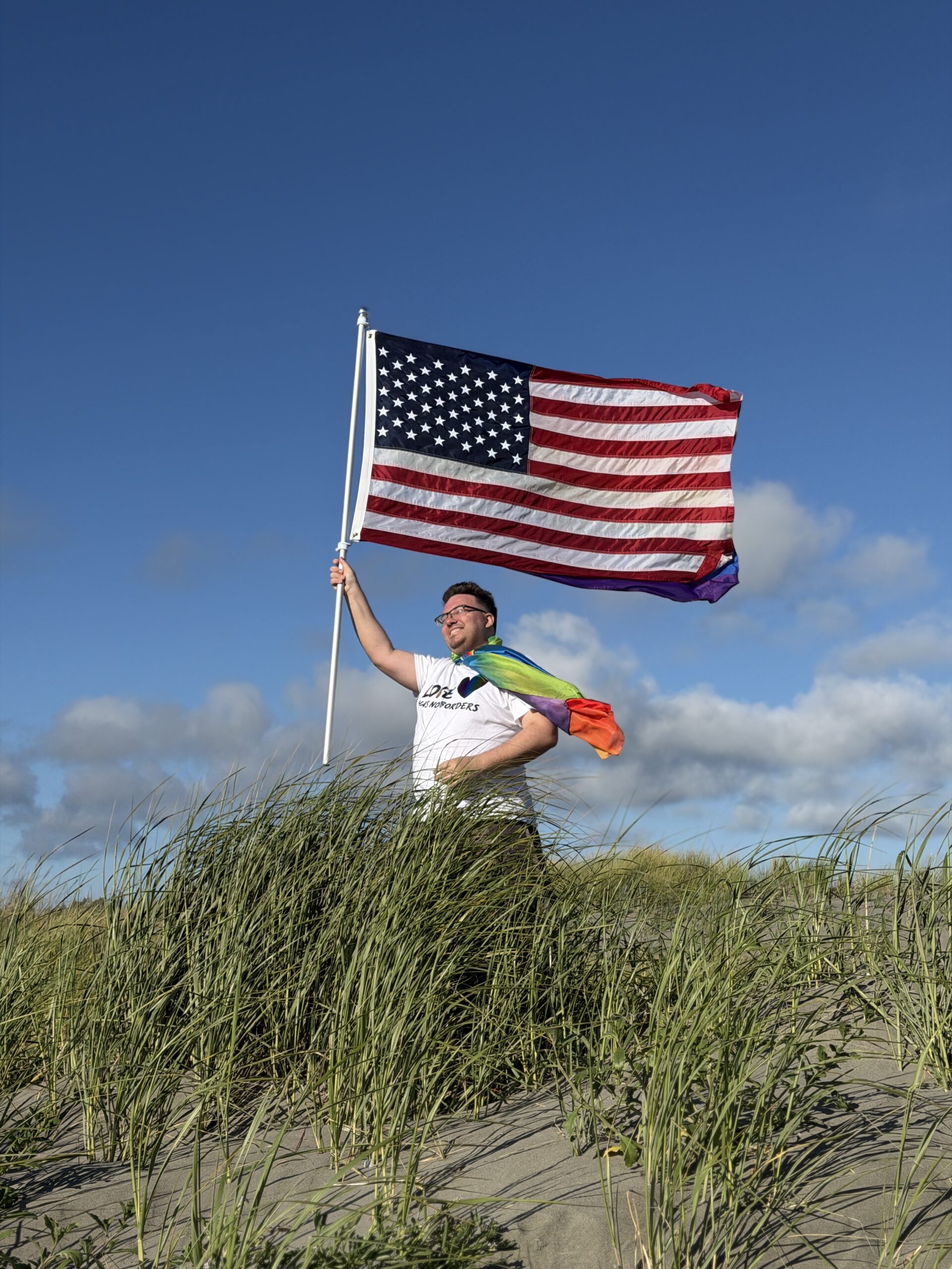 Кевин Дюк с флагами США и ЛГБТ на берегу Тихого океана в Ocean City, штат Вашингтон